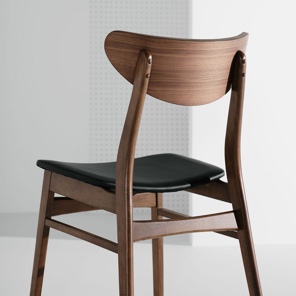 Des lignes douces, des courbes souples et un coussin d'assise en cuir artificiel noir élégant et ajusté confèrent une touche de raffinement à la structure en bois finement travaillé à la chaise Colby de Nuevo.