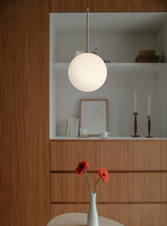 La lampe suspendue Bola Sphere de Pablo Designs sublime vos pièces avec son globe opalin et son design aérien. laiton
