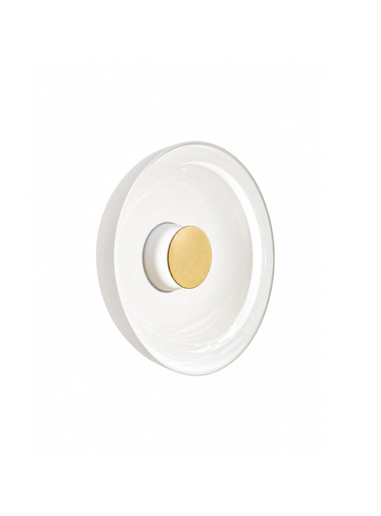 L'applique murale Totem de Pablo Designs crée un halo lumineux raffiné avec son diffuseur en verre opalin. blanc laiton
