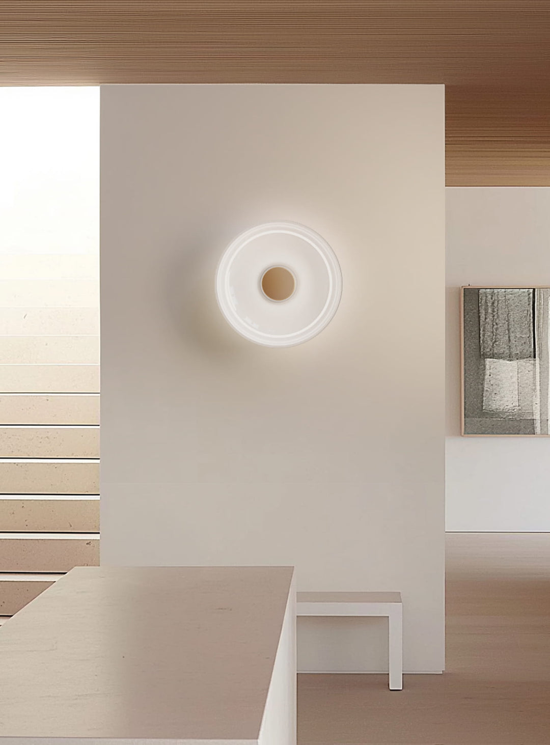 Applique murale Totem de Pablo Designs au design épuré, avec un halo lumineux doux projeté sur le mur. gris laiton