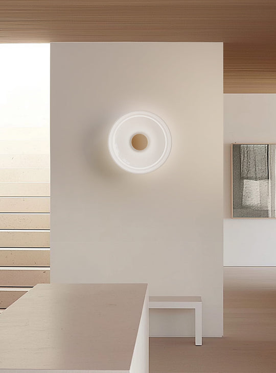 Applique murale Totem de Pablo Designs au design épuré, avec un halo lumineux doux projeté sur le mur. gris laiton