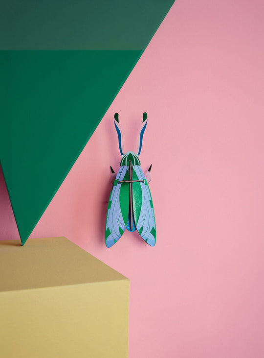 Décoration murale Sauterelle Jade Studio Roof, un insecte 3D en carton recyclé aux reflets verts et bleus.