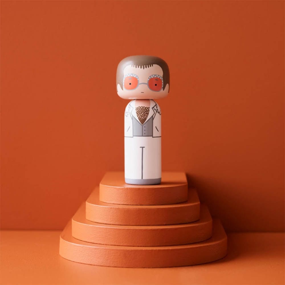 Explorez la poupée Kokeshi d'Elton John, une création exceptionnelle par Lucie Kaas. Capturant l'excentricité légendaire du roi de la pop, cette figurine en bois est un hommage vivant à une icône musicale.