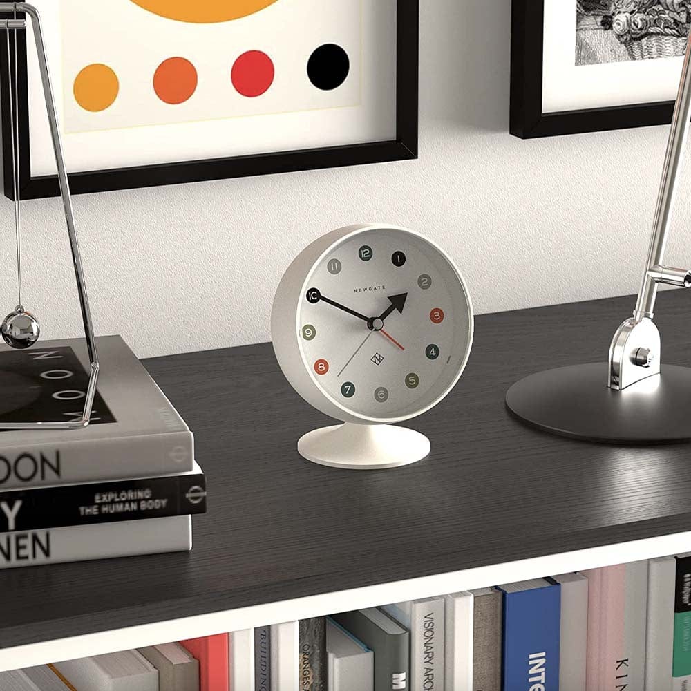 Un réveil sphérique du style des années 1970 par Newgate avec un cadran incliné à points arabes et des aiguilles en métal. L'horloge et le support en acrylique ont une finition mate, avec une lentille en acrylique, et une alarme sonore numérique.