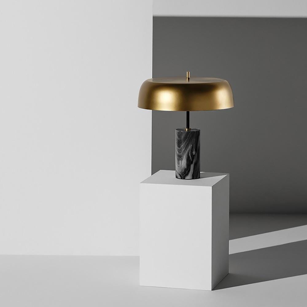 La lampe de table Maddox évoque une esthétique sculpturale unique. Une base cylindrique en marbre noir supporte une nuance de laiton mat en offset, alliant des matériaux riches et vibrants à la fonction et à la forme.