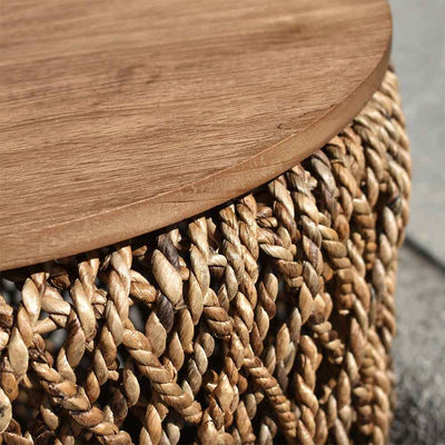 La table d’appoint Knut : polyvalence artisanale et charme rustique. Fabriquée à la main avec de l'abaca durable et du fer, son plateau amovible en teck recyclé offre un rangement élégant et pratique.